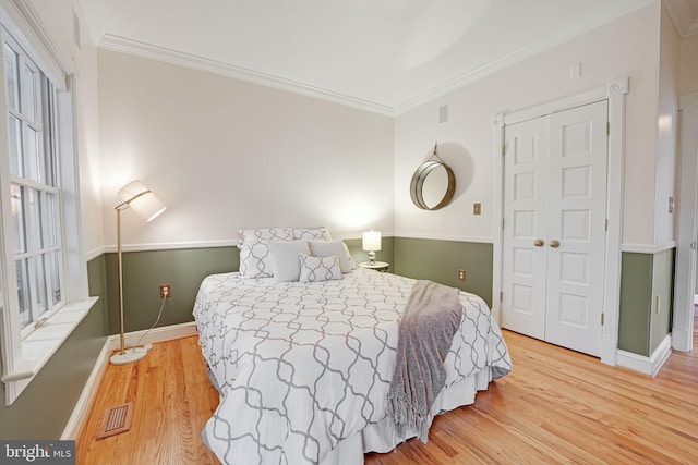 bedroom with light wood-style floors, baseboards, visible vents, and crown molding