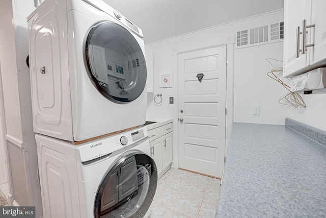 washroom with stacked washer / drying machine, cabinet space, and light tile patterned floors