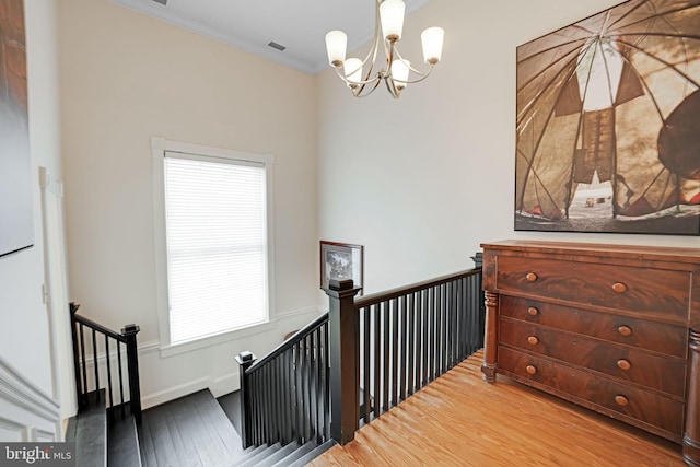 staircase with a chandelier, ornamental molding, and wood finished floors