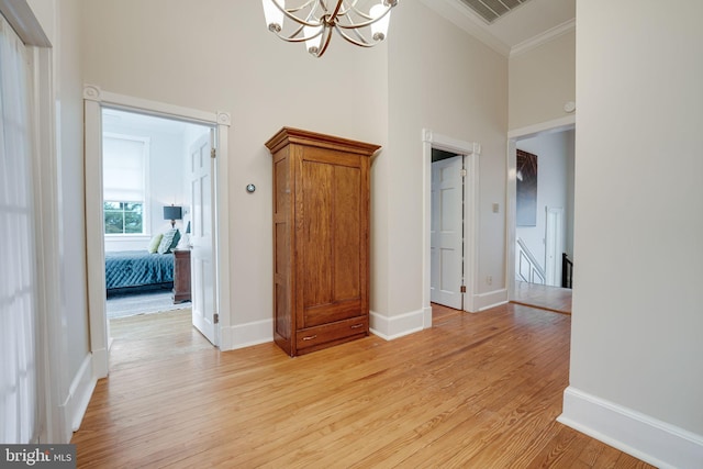 interior space featuring visible vents, ornamental molding, a high ceiling, light wood-type flooring, and a notable chandelier