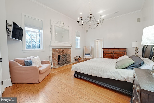 bedroom featuring light wood-style floors, a brick fireplace, crown molding, and an inviting chandelier