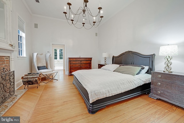 bedroom with a chandelier, light wood-style flooring, a towering ceiling, ornamental molding, and a brick fireplace