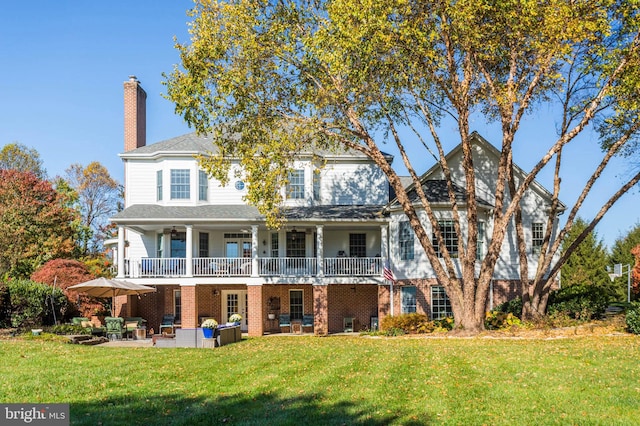 rear view of property with a patio, brick siding, a lawn, and a chimney