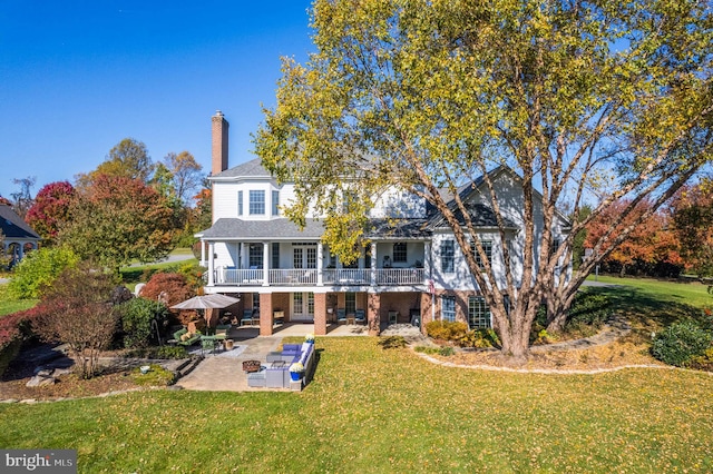 back of property with a yard, a chimney, a patio, and a balcony