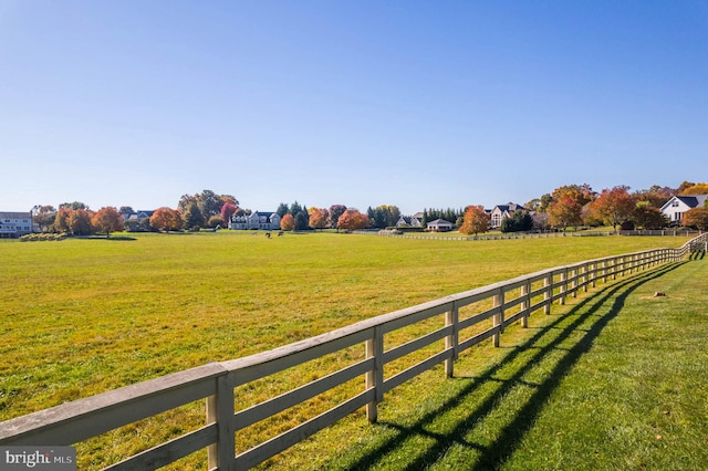 view of community with fence, a lawn, and a rural view