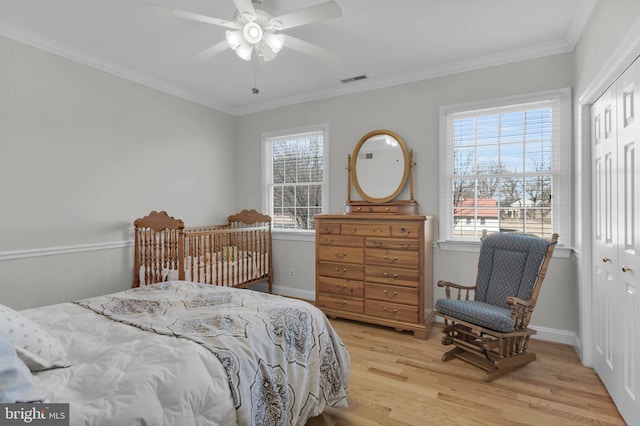 bedroom featuring light wood-style flooring, multiple windows, ornamental molding, and a closet