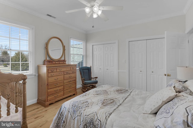 bedroom with light wood-type flooring, crown molding, visible vents, and two closets