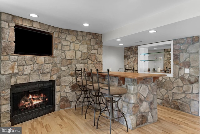 bar with recessed lighting, wood finished floors, indoor wet bar, and a stone fireplace