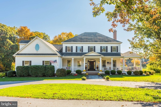 colonial inspired home with roof with shingles, a porch, a front lawn, and a chimney