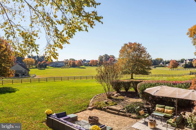 view of yard featuring an outdoor living space with a fire pit, a patio area, a rural view, and fence