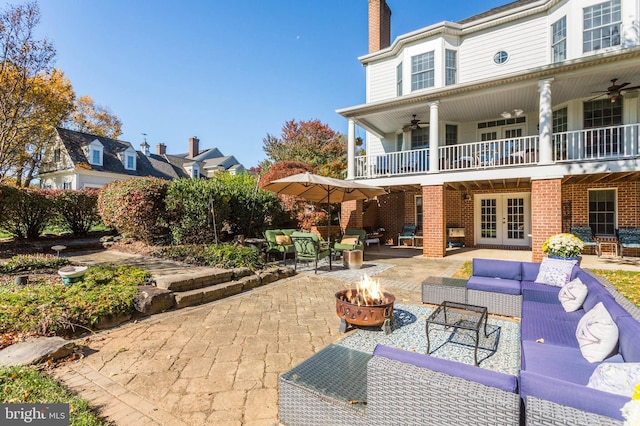 view of patio / terrace featuring a balcony, an outdoor living space with a fire pit, a ceiling fan, and french doors