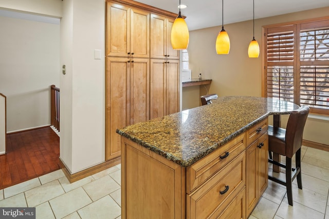 kitchen with light tile patterned flooring, a breakfast bar, dark stone counters, hanging light fixtures, and a center island