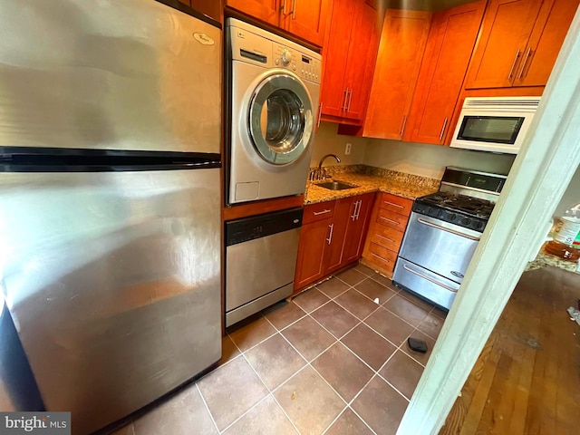 kitchen with light stone counters, stacked washer / drying machine, sink, stainless steel appliances, and tile patterned flooring