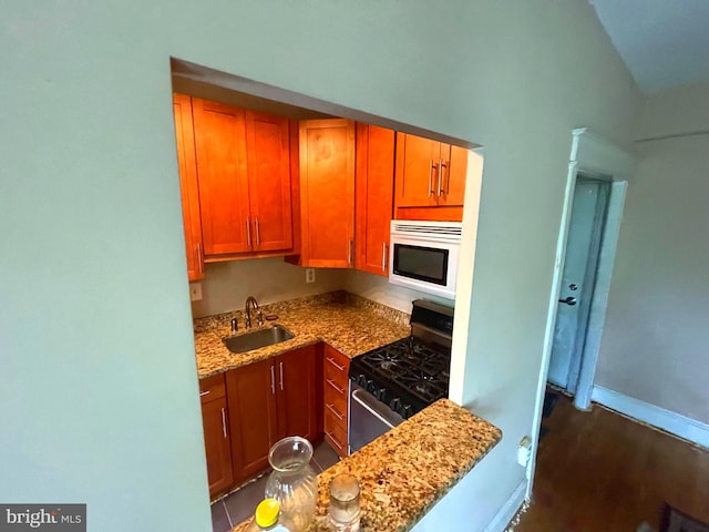 kitchen with dark tile patterned flooring, light stone counters, stainless steel gas stove, and sink