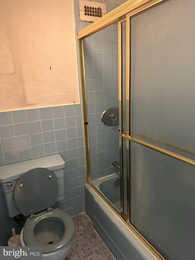 bathroom featuring toilet, combined bath / shower with glass door, tile walls, and tile patterned floors