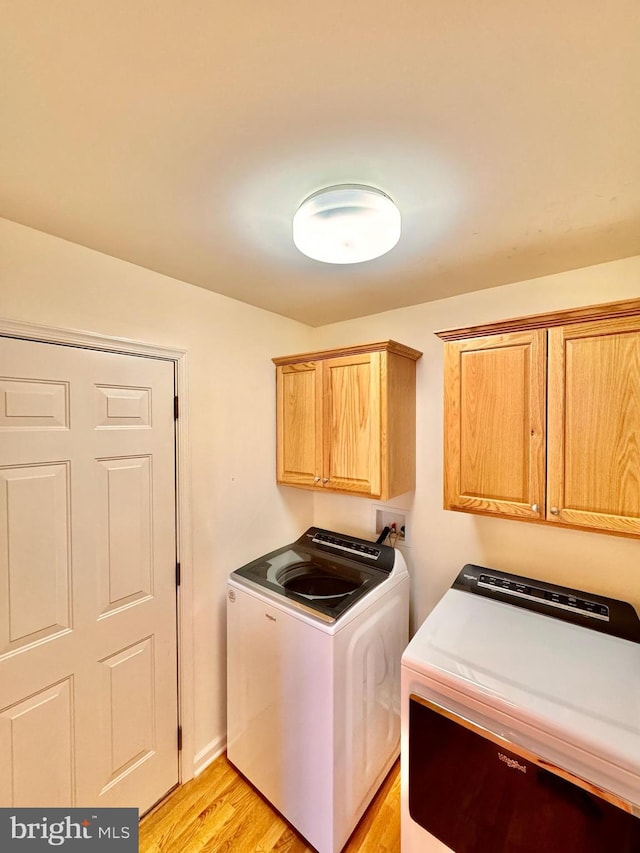 washroom featuring washer and dryer, cabinets, and light wood-type flooring