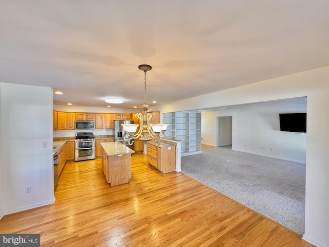 kitchen with light stone countertops, a center island, hanging light fixtures, light hardwood / wood-style flooring, and appliances with stainless steel finishes