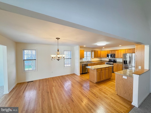 kitchen featuring sink, appliances with stainless steel finishes, pendant lighting, a kitchen island, and light wood-type flooring