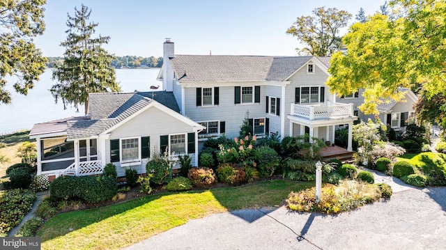 view of front facade with a front lawn, a chimney, a water view, and a balcony