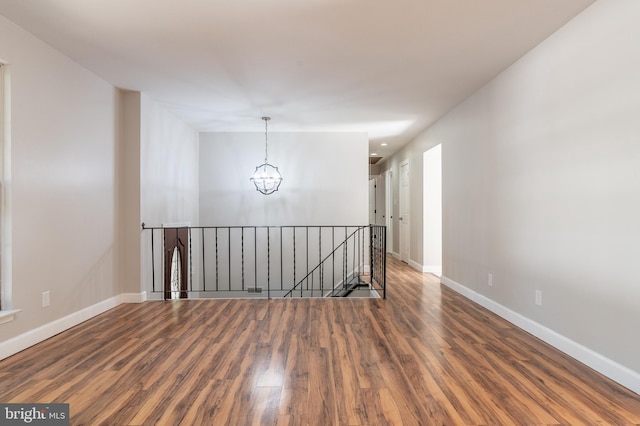 spare room with a notable chandelier and dark hardwood / wood-style flooring