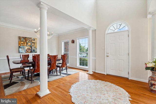 entryway featuring crown molding, ornate columns, wood-type flooring, and an inviting chandelier