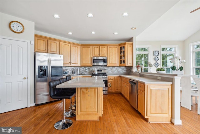 kitchen with backsplash, appliances with stainless steel finishes, a kitchen bar, light hardwood / wood-style floors, and a center island