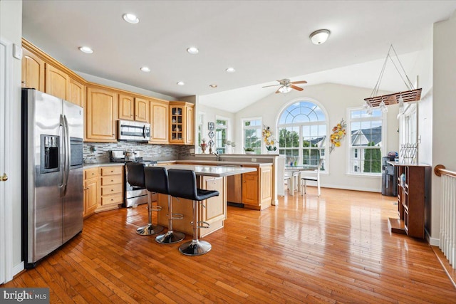 kitchen featuring a kitchen island, light hardwood / wood-style flooring, stainless steel appliances, a breakfast bar, and vaulted ceiling