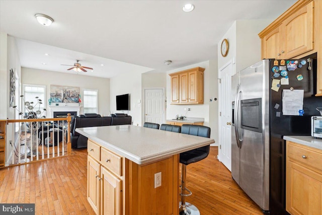 kitchen featuring a kitchen island, light hardwood / wood-style flooring, a breakfast bar, stainless steel fridge with ice dispenser, and ceiling fan