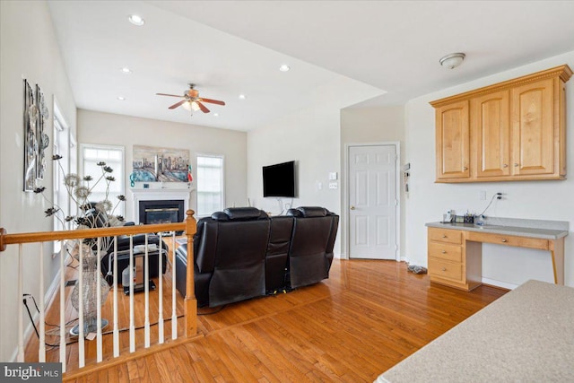 living room featuring built in desk, light hardwood / wood-style floors, and ceiling fan