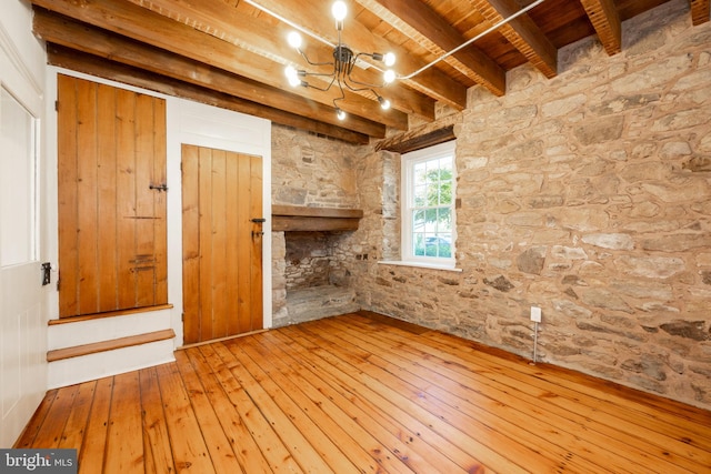 spare room featuring beam ceiling, an inviting chandelier, hardwood / wood-style flooring, wooden ceiling, and a fireplace