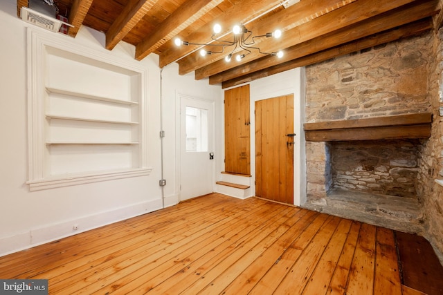 unfurnished living room featuring hardwood / wood-style flooring, a chandelier, beamed ceiling, built in features, and a stone fireplace