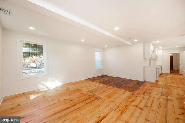 empty room with light wood-type flooring, beamed ceiling, and plenty of natural light