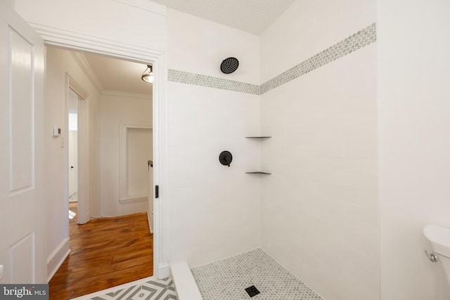 bathroom featuring a tile shower, toilet, crown molding, and wood-type flooring