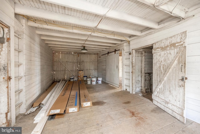 interior space featuring beam ceiling, hardwood / wood-style flooring, wooden walls, and a barn door