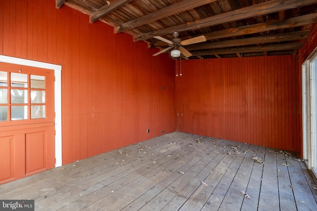 spare room featuring ceiling fan, beamed ceiling, wooden walls, and hardwood / wood-style floors