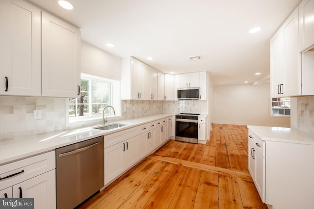 kitchen with light hardwood / wood-style floors, appliances with stainless steel finishes, sink, and white cabinets