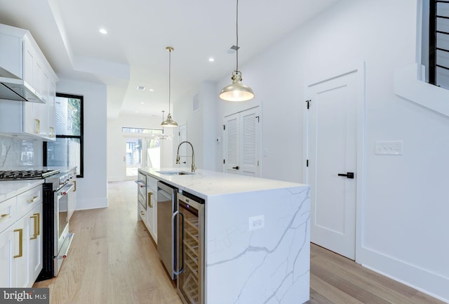 kitchen with a center island with sink, stainless steel stove, hanging light fixtures, sink, and white cabinets