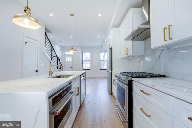 kitchen featuring appliances with stainless steel finishes, hanging light fixtures, wall chimney exhaust hood, and white cabinets