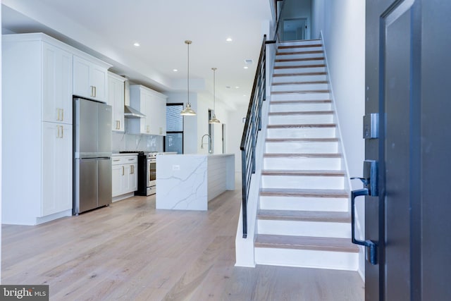 kitchen with stainless steel appliances, a center island with sink, decorative light fixtures, and white cabinetry