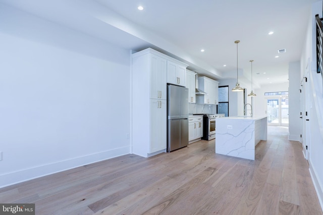 kitchen featuring stainless steel appliances, light hardwood / wood-style floors, white cabinets, an island with sink, and decorative light fixtures