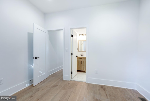 unfurnished bedroom with light hardwood / wood-style flooring, sink, and ensuite bath