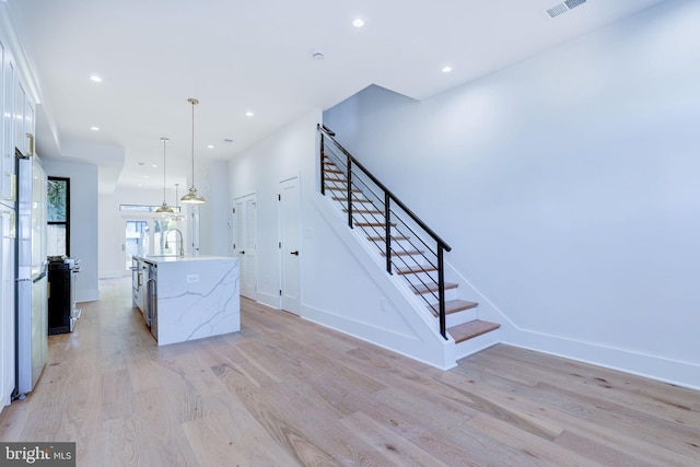 kitchen with a kitchen island with sink, light hardwood / wood-style floors, hanging light fixtures, and white cabinets