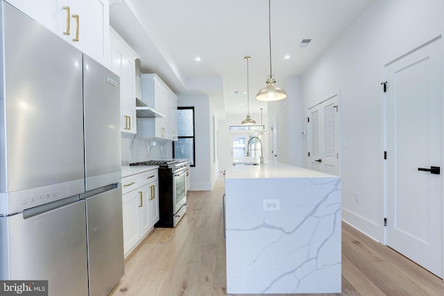 kitchen featuring a center island with sink, stainless steel appliances, light wood-type flooring, white cabinetry, and pendant lighting