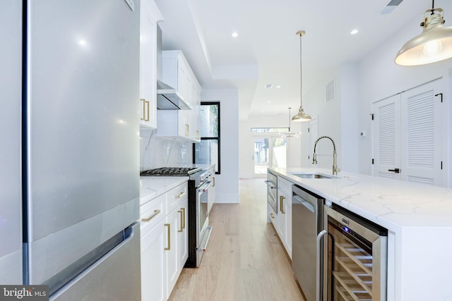 kitchen featuring beverage cooler, white cabinets, an island with sink, appliances with stainless steel finishes, and decorative light fixtures