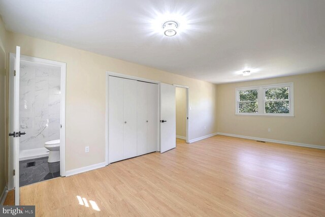 unfurnished bedroom with a closet, ensuite bath, and light wood-type flooring