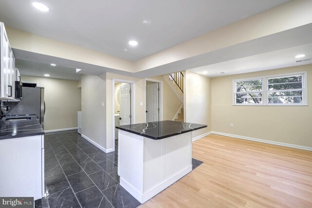 kitchen with kitchen peninsula, stainless steel fridge, white cabinets, a breakfast bar area, and dark wood-type flooring