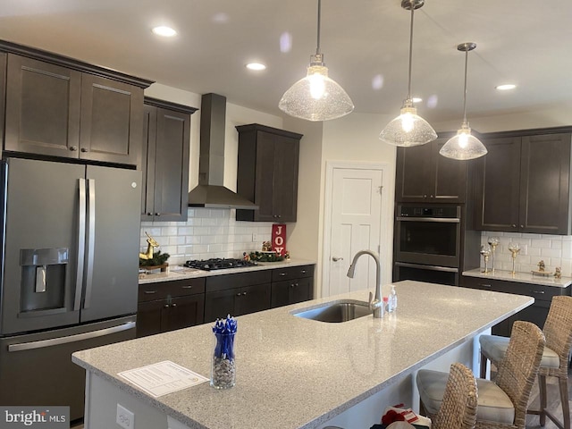 kitchen featuring backsplash, wall chimney exhaust hood, stainless steel appliances, a kitchen island with sink, and sink