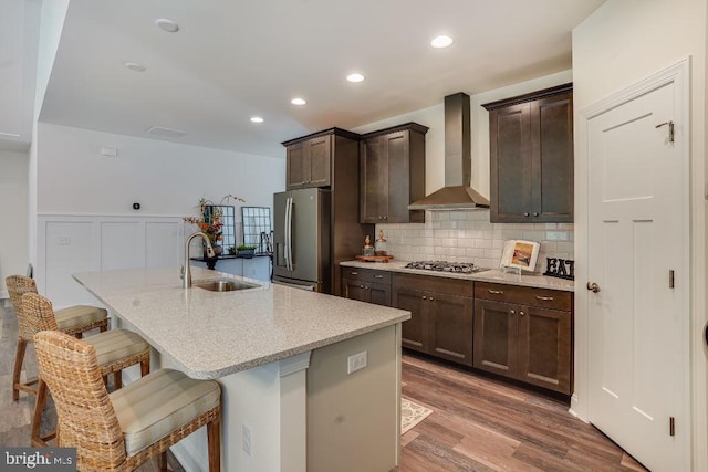 kitchen with sink, stainless steel appliances, wall chimney range hood, a breakfast bar area, and a center island with sink