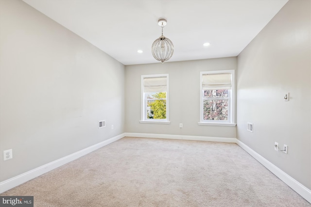 spare room featuring a notable chandelier and light colored carpet