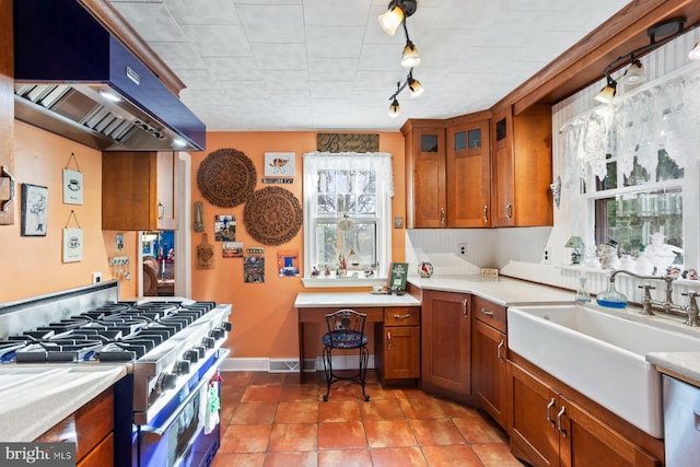 kitchen featuring track lighting, wall chimney exhaust hood, high end stainless steel range oven, sink, and light tile patterned floors